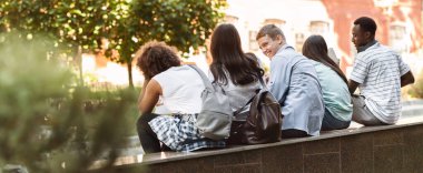 Bir grup neşeli kolej öğrencisinin dersten sonra dışarıda dinlenmesi, sohbet etmesi ve gülmesi.