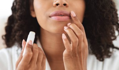 Dudak kremi. Tanımlanamayan siyah kadın dudaklarına nemlendirici ruj sürüyor, kırpılmış görüntü, yakın plan.