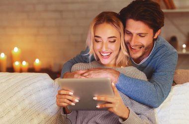 Dijital tablet kullanan mutlu çift akşam evde kanepede oturan film izliyor. Boş Alan