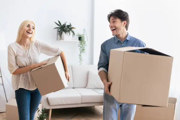 stock image A couple happily carries boxes into their new home, smiling and laughing together.