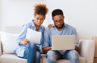 House 'u satın almak. Ciddi Siyahi Çift Dizüstü bilgisayar okuyarak Mülkiyet Kağıtlarını Yeni Evdeki Koltukta Otururken Kullanıyor. Boş Boşluk