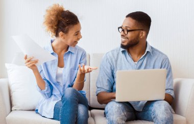 Ev satın almak. Taşındıktan sonra koltukta oturan dizüstü bilgisayar okuma kağıtlarını kullanan Afro Çiftin mutluluğu. Boşluğu Kopyala