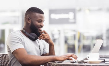 Kulaklık takan bir adam kafe masasında oturur ve dizüstü bilgisayarıyla çalışır..