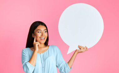 Uzun siyah saçlı genç bir Asyalı kadın pembe arka plan önünde boş bir konuşma baloncuğu tutarken gülümsüyor. Boş konuşma balonu kendi metin veya mesajınızı eklemek için bir fırsat sağlar.