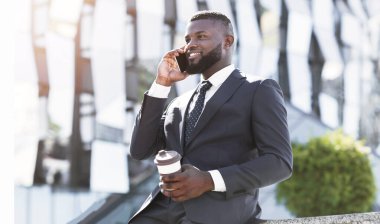 Her zaman temas halinde. Neşeli Afro İşadamı Cep Telefonu Holding Kahve Fincanı Kentsel Alanda Açık Oturan Talking. Boş Alan