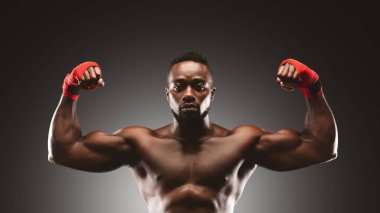 Kırmızı eli olan gömleksiz bir adam stüdyo ortamında pazılarını esnetir..