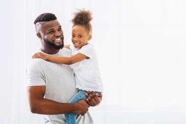 Afrika kökenli Amerikalı baba ve kızı parlak, beyaz bir odada birbirlerine yakın dururlar. Baba, genç kızını kollarında tutarken gülümsüyor. Kız ona neşeli bir ifadeyle bakıyor.