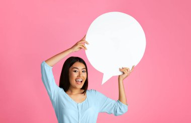 Uzun siyah saçlı genç bir Asyalı kadın gülümsüyor ve pembe bir arkaplan önünde büyük, boş bir konuşma balonu tutuyor.