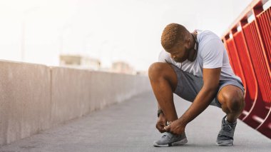 Köprüde koşu ayakkabısı bağlayan siyah bir adam.