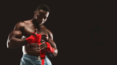 Kaslı bir boksör dövüş hazırlığı için ellerini kırmızı bant ile sarar..