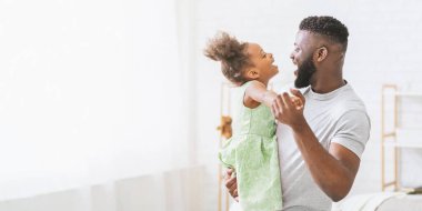 Mutlu bir Afrikalı Amerikalı baba ve kızı parlak ve ferah bir oturma odasında dans ediyorlar. Onlar gülüyor ve gülüyorlar. Eğlenceli danslarından zevk alıyorlar, kopyalama alanından.