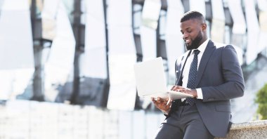 Şehir merkezindeki kahve molası sırasında dizüstü bilgisayar kullanarak internet kullanan mutlu Afrikalı Amerikalı girişimci.