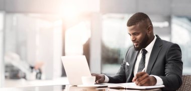 Ciddi Afro İşadamı Laptop Açık Kafede Kahve Molası Sırasında Notlar Alarak Çalışma. Meşgul Gün Konsepti