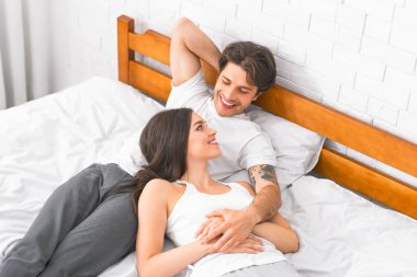 Genç bir çift yatak odasında birlikte yatıyor. Adam gülümsüyor ve yüzünde bir gülümseme ile ona bakan kadına bakıyor. İkisi de gündelik kıyafetler giyiyor.