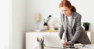 Dişi girişimci bilgisayardaki iş e-postalarına cevap veriyor, işyerinin yanında duruyor.