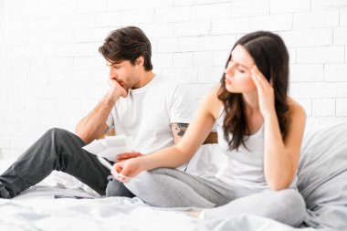 Bir adam ve bir kadın yatakta oturmuş sıkıntılı görünüyorlar. Adam elinde bir kağıt parçası tutuyordu, ve kadın da yere bakıyordu. İkisi de sıkıntılı ya da endişeli görünüyor..