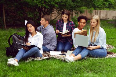 Üniversite kampüsünde okuyan, dizüstü bilgisayar kullanan, kitap okuyan, derslere hazırlanan bir grup öğrenci.