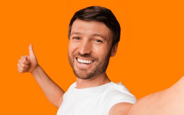 Gibi. Gülümseyen Adam Selfie Çekiyor. Sarı arka planda duran bir şeyi onaylıyor. Stüdyo Çekimi