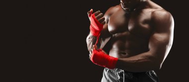 Kaslı bir adam antrenman için ellerini kırmızı boks bandıyla sarar..