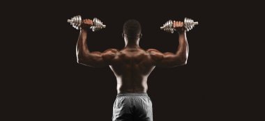 Kas yığını bir adam spor salonundaki dambılları kaldırır, sırtı kameraya dönük..