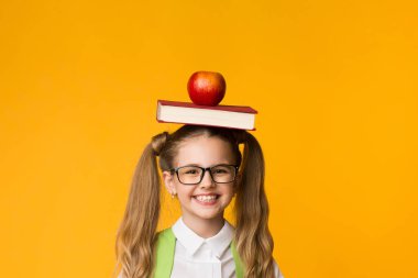Smile Schoolgirl Gesturing Thumbs-Up Holding Kitap ve Stüdyoda Sarı Arka Plan Üzerinde Baş Apple. Boş Alan