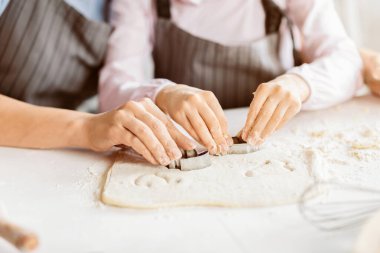 Hamurdaki şekilleri kesmek için bir çift eli kesmiş. Hamur ince bir un katmanıyla kaplıdır ve kurabiye kesiciler hamurda küçük, mükemmel daireler bırakır.