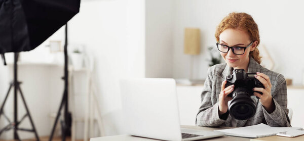 Женщина в студии, внимательно осматривающая камеру в руках.