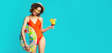 Yaz kokteyli ve yüzme halkası tutan mayo içinde Mutlu bin yıllık Afrikalı Amerikalı kadın, mavi stüdyo arka plan
