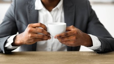 Afrika kökenli Amerikalı iş adamı işyerinde kahve içiyor, modern ofiste mola veriyor. Yakın çekim, ellere odaklanma