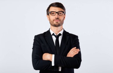 Siyah takım elbiseli profesyonel bir adam kollarını kavuşturup doğrudan kameraya bakar. Beyaz gömlek ve siyah kravat giyiyor..