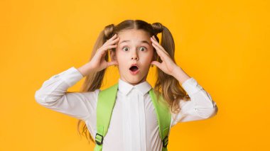 Oops, Okul Son Teslim Tarihi. Şok İlköğretim Öğrenci Kız Tutarak Head Sarı Stüdyo Arka Plan Üzerinde Kamera Bakıyor.