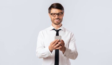 Gözlüklü ve siyah kravatlı beyaz gömlekli bir adam telefonuna bakarken gülümsüyor..