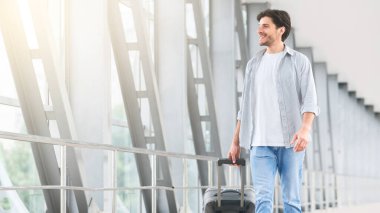 Havaalanı yürüyüşü. Terminalde yürüyen, bavullu yakışıklı genç adam, biniş kapısına gidiyor.