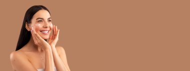 Güzel, çıplak esmer, uzun saçlı genç bir kadın yüzüne güzellik ürünleri sürüyor ve gülümsüyor. Fotokopi odasına bakıyor. Bej renkli stüdyo arka planında izole edilmiş, göz kremi kullanıyor.