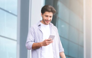 Taksi çağırıyorum. Millennial Guy, Bavul Havalimanı 'nın yanında dururken akıllı telefon kullanıyor, uçuştan sonra açık havada dinleniyor,