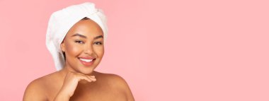 Spa konseptinden sonra. Kafasında banyo havlusu olan tombul zenci kadın portresi ve kameraya gülümseyen parlak cilt, güzellik tedavisinden sonra mutlu olmak, pembe stüdyo arka planı, fotokopi alanı.