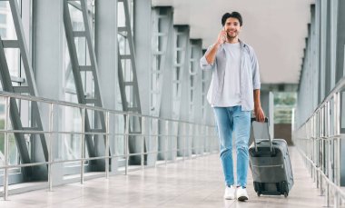 Telefonla konuşan genç turist, havaalanında bagajda yürüyor, boş alan