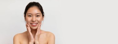 Mutlu Asyalı genç bayan yanaklarına dokunuyor ve kameraya gülümsüyor, Koreli kadın cilt bakımını seviyor, beyaz stüdyo arkaplanının başında duruyor,