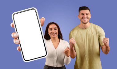 Genç bir kadın, bir erkekle kutlama yaparken önünde beyaz bir ekranla akıllı bir telefon tutuyor. Adam yumruklarını havaya kaldırdı ve gülümsüyor..