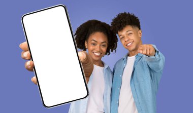 Genç siyah bir kadın ve erkek yan yana duruyor, gülümsüyor ve kamerayı işaret ediyorlar. Önlerinde boş ekran olan bir akıllı telefon tutuyorlar. Arkaplan açık mavi renkte..