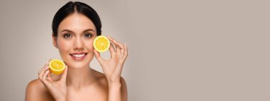 Mükemmel yüzlü, pozitif beyaz bir bayan, sarı limon meyveleri gösteriyor, gri stüdyo arka planında izole edilmiş. C vitamini tavsiye, güzellik ve cilt bakımı, gençleştirici, kopyalama alanı