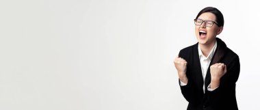 Siyah takım elbiseli ve gözlüklü bir kadın, yumruklarını sıkmış, heyecandan bağırıyor. Büyük bir başarıyı kutluyor gibi görünüyor..