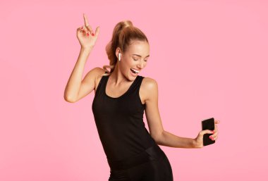 Egzersiz çalma listesi. Akıllı telefon tutan genç kadın sarı stüdyo arka planda müzik dinleyerek dans ediyor. Boş alan