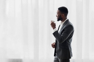 Neşeli Afrikalı Amerikalı işadamı ofiste pencere yakınında kahve içme başarılı anlaşma sonra heyecanlı, kopya alanı