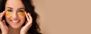 Mutlu genç bir kadın göz bandı takıyor, bej arka planda işlemlerin tadını çıkarıyor, stüdyo çekimi yapıyor. Cilt bakımı, doğal güzellik, kaplıca tedavisi konsepti, kopyalama alanı