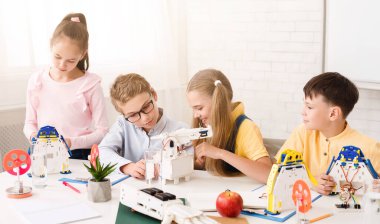 Dört çocuk, üç erkek ve bir kız, bir sınıf ortamında robotlar üzerinde çalışıyorlar. Hepsi görevlerine odaklanmış ve eğleniyor gibi görünüyorlar. Sınıf parlak.