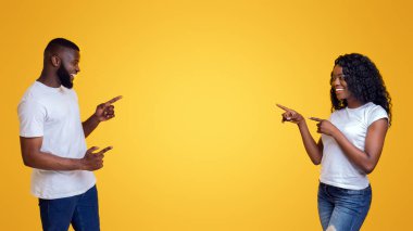 Neşeli siyah çift gülümseyerek ve neşeyle uzak boş alan, sarı arka plan işaret