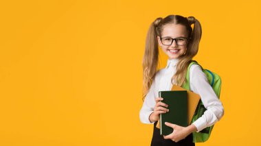 Okula döndüğün için mutluyum. Neşeli İlköğretim Öğrencisi Kız Stüdyoda Sarı Arka Plan Üzerinde Poz Kitaplar Holding. Kopyalama Alanı