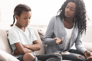 İtaatsiz çocuk. Katı siyah anne küçük kızına azarlayarak bakıyor, evdeki kanepede oturuyor, yakın plan.