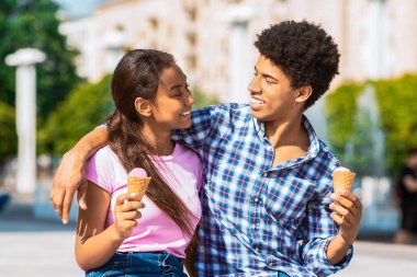 Genç siyahi bir çift şehir ortamında oturmuş, ellerinde dondurma külahları var. Birbirlerine bakıp gülümsüyorlar. Sıcak ve güneşli bir günde birbirlerine eşlik ediyorlar..